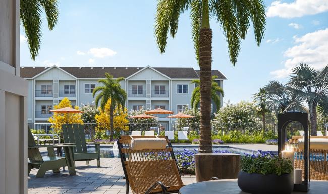 a patio with chairs and tables with umbrellas palm trees and a building in the background